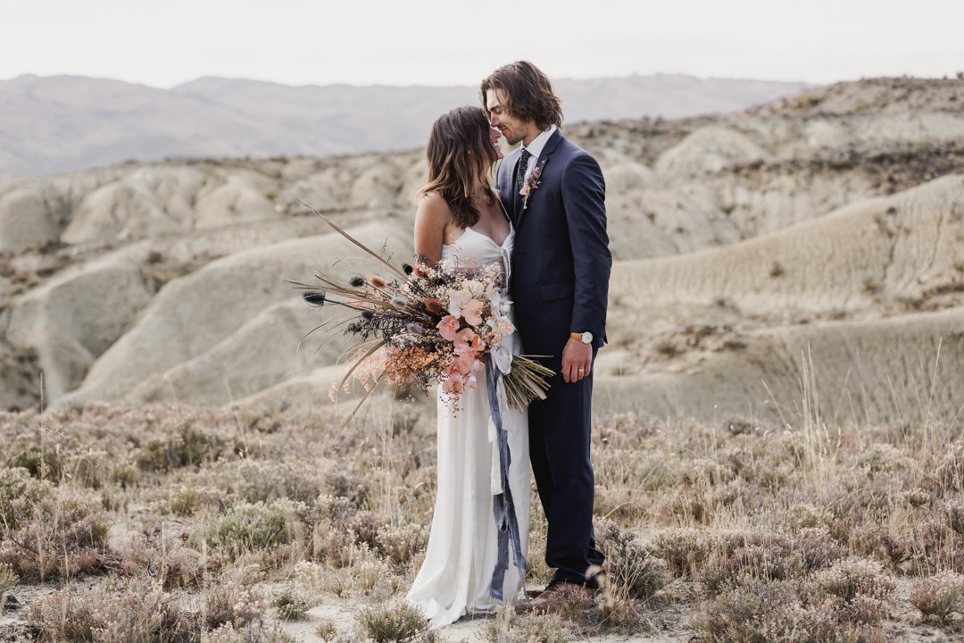Bride wearing modern bohemian wedding gown by L'eto Bridal with sweeping maxi skirt and bow tie combo and groom wearing Sergio's Menswear blue suit